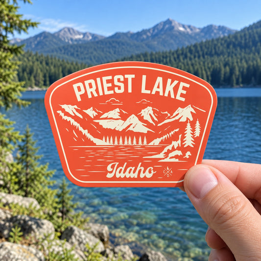 Classic Priest Lake Idaho sticker held outdoors beside a clear mountain lake