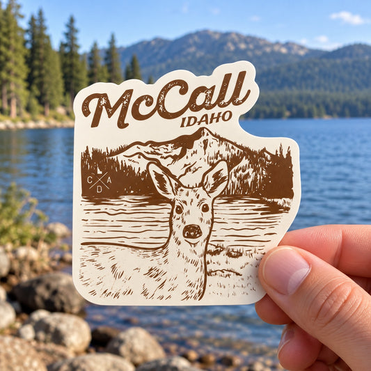 McCall Idaho Oh Deer sticker held outdoors by Payette Lake