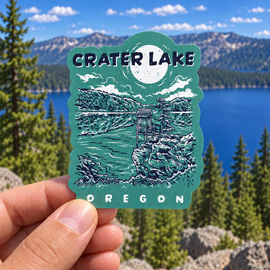 Cleetwood Cove Trail Crater Lake sticker held outdoors above a blue mountain lake