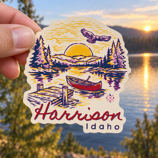 Classic Harrison Canoe sticker held outdoors above a North Idaho lake at sunset